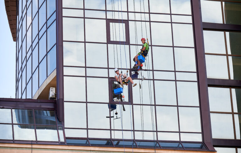 Industrial mountaineering worker cleaning window outside building.